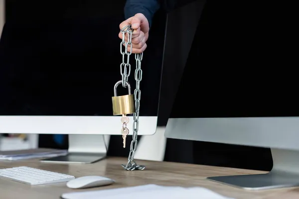 Vue recadrée du programmeur tenant cadenas sur la chaîne près des ordinateurs dans le bureau — Photo de stock