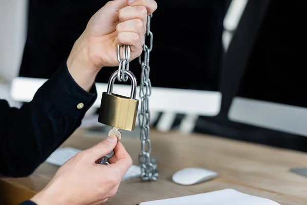 Vue recadrée du programmeur tenant cadenas et clé près des ordinateurs flous dans le bureau — Photo de stock