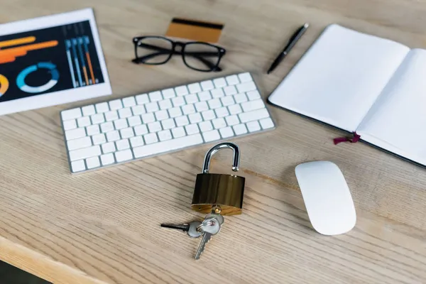 Padlock with keys near computer mouse, keyboard and notebook on table — Stock Photo