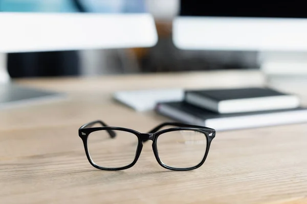 Gafas en la mesa cerca de portátiles y ordenadores en la oficina - foto de stock