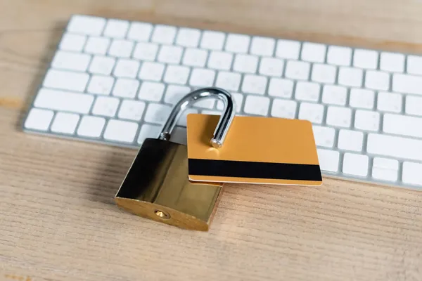 Nahaufnahme der Kreditkarte im Vorhängeschloss in der Nähe der Tastatur auf einem Holztisch — Stockfoto