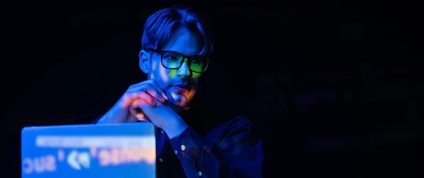 Young developer in eyeglasses near laptop with code reflection isolated on black, banner — Stock Photo