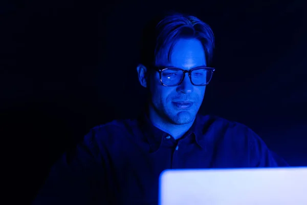Desenvolvedor em óculos olhando para laptop borrado isolado em preto — Fotografia de Stock