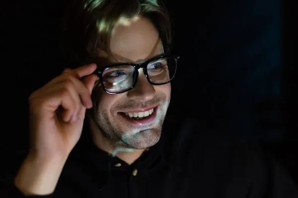 Homme souriant avec reflet lumineux du visage tenant des lunettes isolées sur noir — Photo de stock