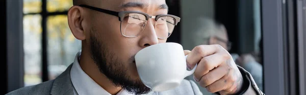 Close up view of asian businessman in eyeglasses drinking coffee in office, banner — Fotografia de Stock