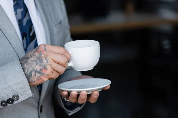 Visão parcial de homem de negócios com tatuagem segurando xícara de café no escritório — Fotografia de Stock