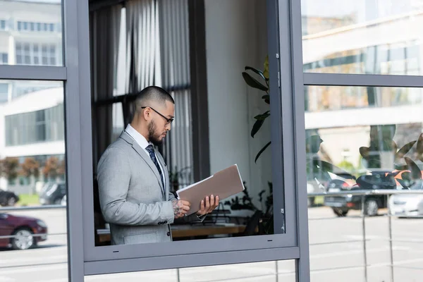 Asiático hombre de negocios en formal desgaste y gafas lectura de documentos cerca de ventana abierta - foto de stock