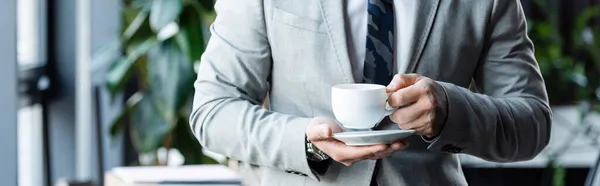 Vista parcial del hombre de negocios en ropa formal sosteniendo taza de café en la oficina, pancarta - foto de stock