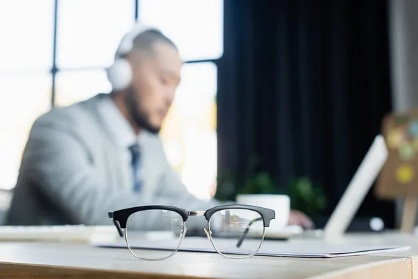 Enfoque selectivo de gafas cerca borrosa asiático hombre de negocios trabajando en la oficina - foto de stock