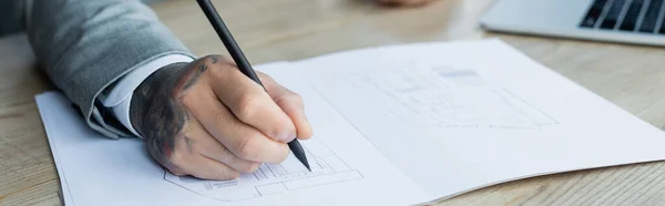 Partial view of tattooed architect drawing blueprint at workplace, banner — Stock Photo