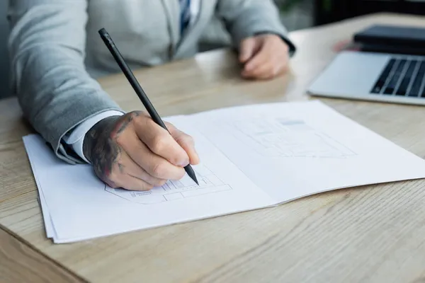 Vue recadrée du plan directeur de dessin d'architecte près d'un ordinateur portable flou sur le bureau — Photo de stock