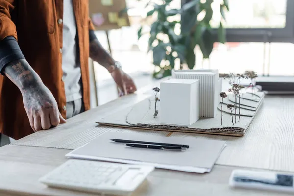 Ausgeschnittene Ansicht des Architekten, der in der Nähe des Arbeitsplatzes mit Hausmodellen, Ordnern und verschwommenem Taschenrechner steht — Stockfoto