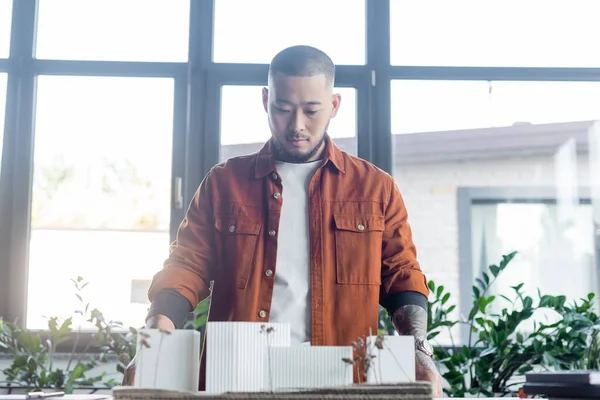 Asian architect holding construction project while standing against windows in office — Stock Photo