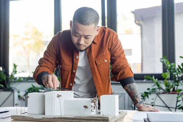 Tätowierter asiatischer Architekt misst Hausmodelle mit Bleistift bei der Arbeit im Büro — Stockfoto