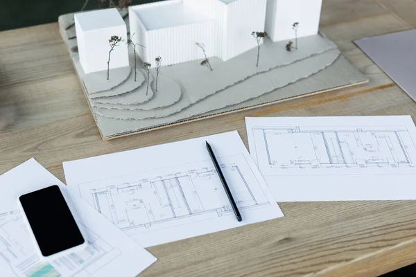 Visão de alto ângulo de planos arquitetônicos, modelos de casa e telefone celular com tela em branco na mesa de madeira — Fotografia de Stock