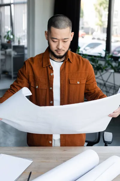 Asiatischer Ingenieur schaut sich Baupläne an, während er im Architekturbüro arbeitet — Stockfoto