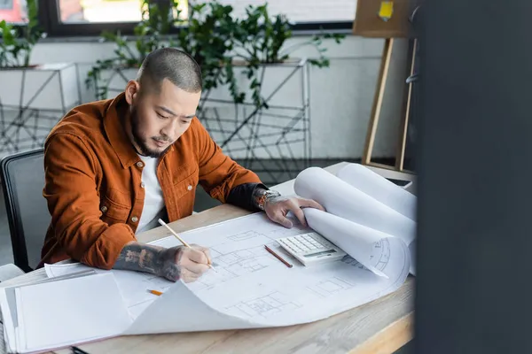 Asiatischer Architekt zeichnet Blaupause, während er im Büro auf verschwommenem Vordergrund arbeitet — Stockfoto