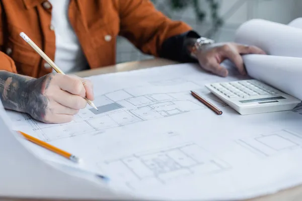 Vista recortada de ingeniero tatuado dibujo plano arquitectónico cerca de la calculadora en el escritorio - foto de stock