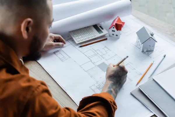 High angle view of blurred asian architect drawing blueprint near house models and calculator — Stock Photo