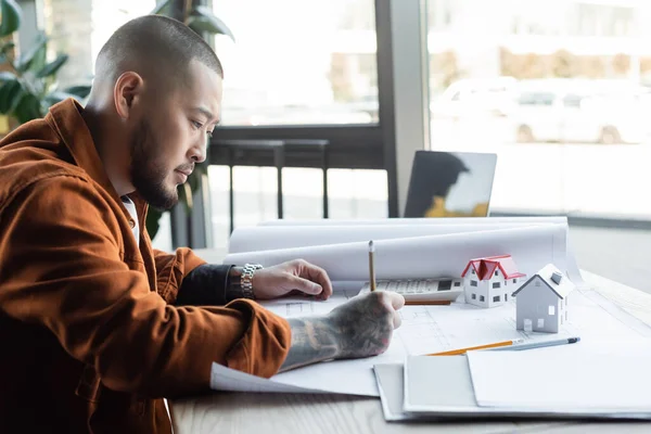 Asiatischer Architekt zeichnet Blaupause während seiner Arbeit an einem Architekturprojekt im Büro — Stockfoto