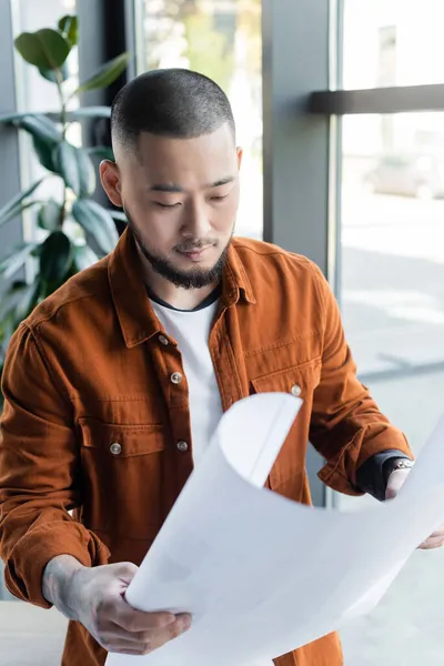 Asiatischer Architekt schaut sich während seiner Arbeit im Büro den Bauplan an — Stockfoto