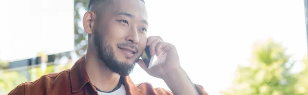 Усміхнений азіатський бізнесмен розмовляє на мобільному телефоні в офісі, банер — стокове фото