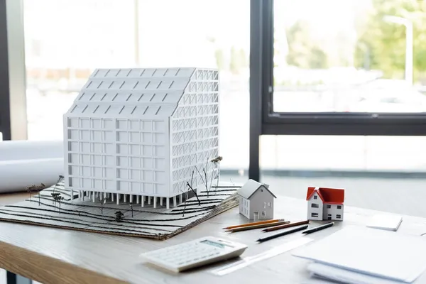 Modèles de maison, crayons et calculatrice floue sur le bureau dans le bureau de construction — Photo de stock