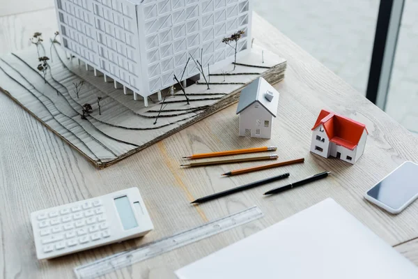 Modelos da casa, lápis, smartphone com tela em branco e calculadora borrada na mesa de madeira no escritório — Fotografia de Stock