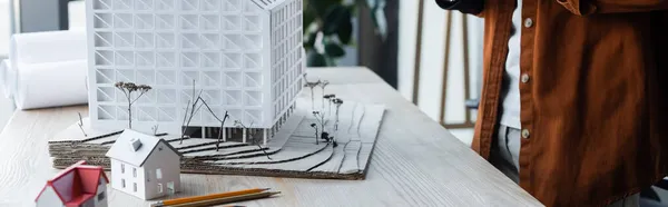 Vue partielle de l'architecte debout près des modèles de maison sur le bureau dans le bureau, bannière — Photo de stock