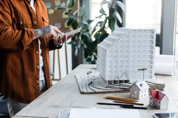 Visão parcial do arquiteto usando calculadora perto de modelos de casa na mesa de trabalho no escritório — Fotografia de Stock