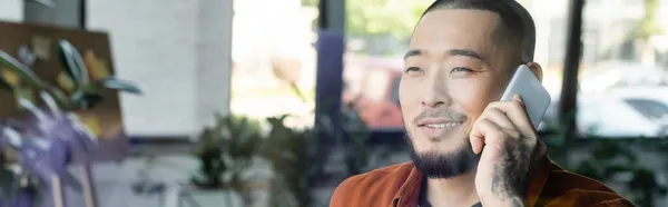 Tatoué asiatique homme d'affaires souriant pendant conversation téléphonique dans bureau, bannière — Photo de stock