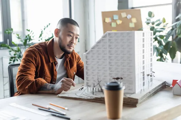 Asian architect working on construction project near blurred takeaway drink — Stock Photo