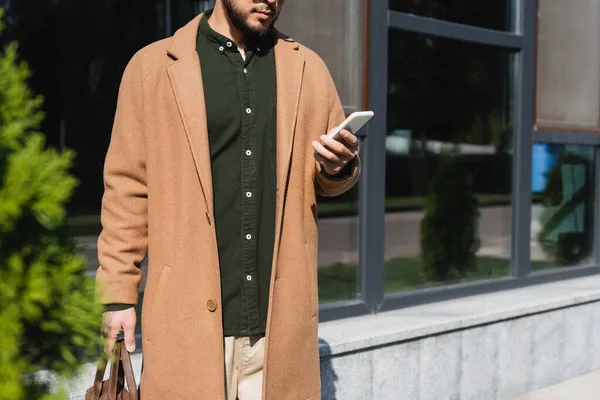Обрізаний вид людини в бежевому пальто, використовуючи смартфон на відкритому повітрі — стокове фото