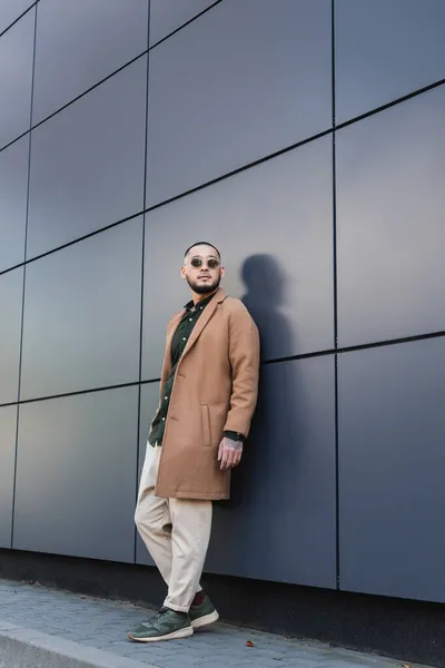 Vista completa dell'uomo asiatico in elegante abito autunnale e occhiali da sole vicino al muro grigio in città — Foto stock