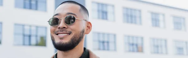 Barbudo ásia homem no moderno óculos de sol sorrindo ao ar livre, banner — Fotografia de Stock