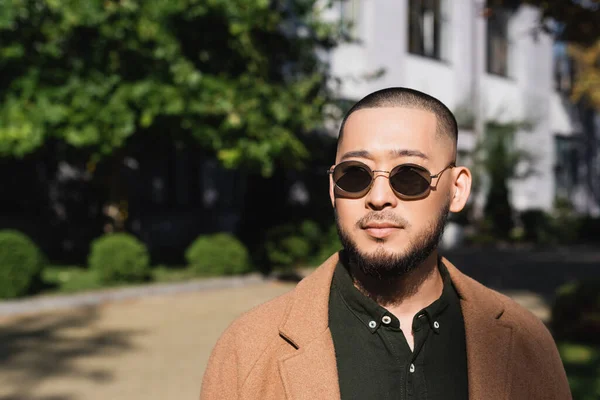 Bearded asian man in beige coat and sunglasses on city street — Stock Photo
