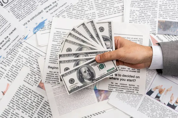 KYIV, UKRAINE - NOVEMBER 1, 2021: top view of man holding dollar banknotes above printed newspapers — Stock Photo