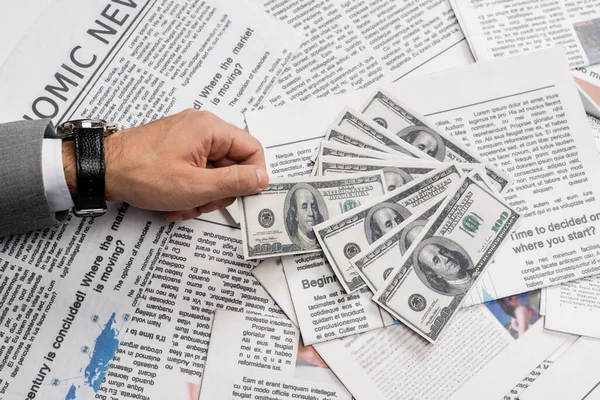 KIEW, UKRAINE - 1. NOVEMBER 2021: Ausgeschnittene Ansicht eines Mannes, der Dollarnoten in der Nähe gedruckter Zeitungen hält — Stockfoto