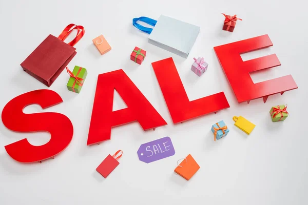 High angle view of sale letters near tiny shopping bags and presents on white — Stock Photo