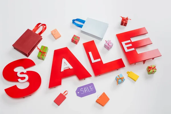 High angle view of red sale letters near tiny shopping bags and presents on white — Stock Photo