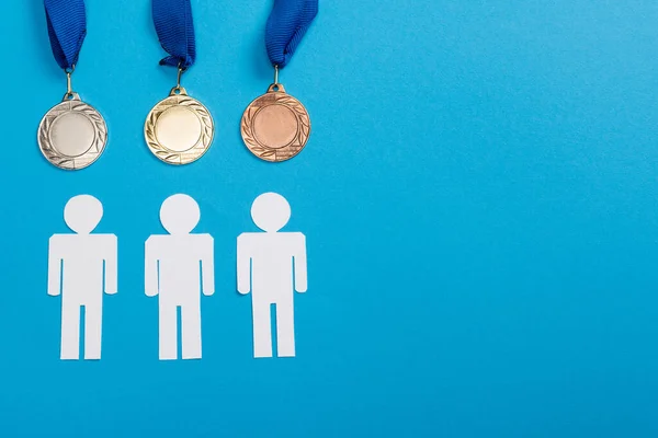 Vue du dessus des personnes coupées en papier blanc près des médailles d'argent et d'or sur bleu — Photo de stock