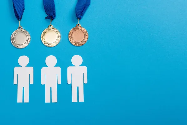 Vue du dessus des personnes coupées en papier blanc près des médailles d'argent et d'or sur bleu — Photo de stock