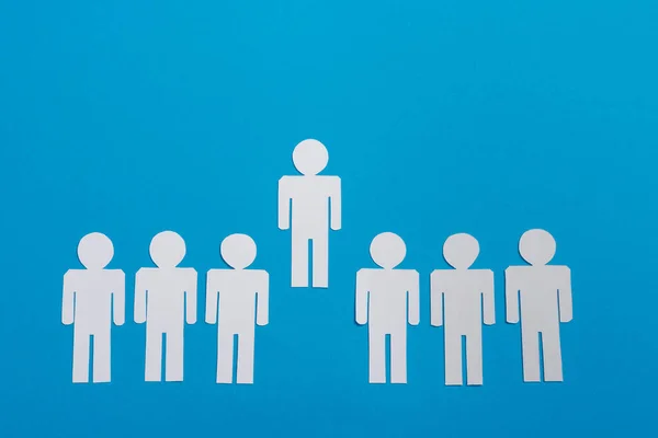 Top view of white paper cut people in line near leader isolated on blue, team concept — Stock Photo