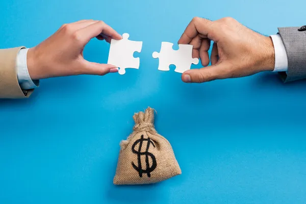 Top view of female and male hands with jigsaw near money bag on blue — Stock Photo