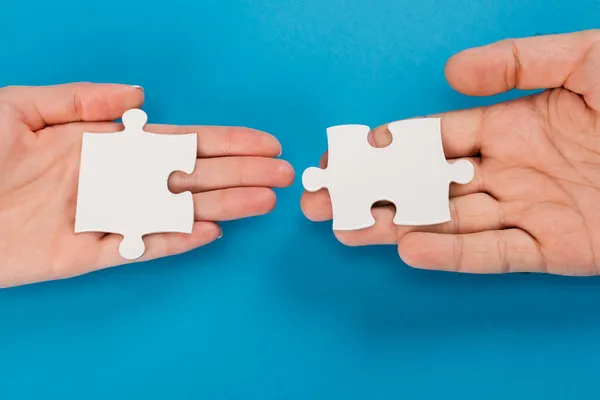 Top view of female and male hands with jigsaw on blue — Stock Photo