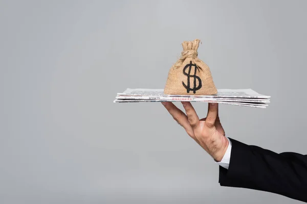 Cropped view of man holding newspapers with money bag isolated on grey — Stock Photo
