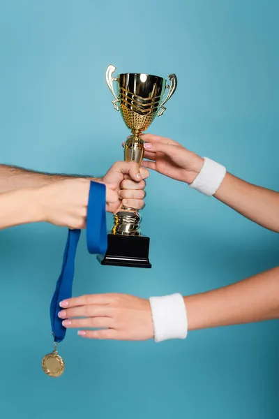 Cropped view of man giving golden trophy and medal to female champion on blue — Stock Photo