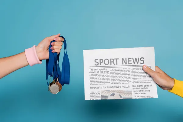 Cropped view of man holding newspaper near woman with medals on blue — Stock Photo