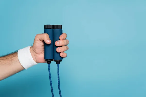 Cropped view of sportsman holding skipping rope on blue — Stock Photo