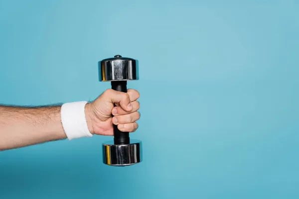 Cropped view of sportsman holding heavy dumbbell on blue — Stock Photo